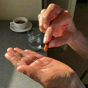 Manos sosteniendo una cápsula blanda de extracto de ajo con un vaso de agua