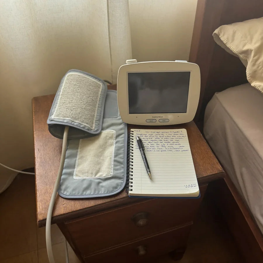 Monitor de presión con la pantalla apagada sobre el buró, junto a una libreta de registros