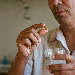 Hombre tomando una cápsula blanda de extracto de ajo con un vaso de agua