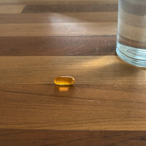 Una sola cápsula blanda sobre la mesa junto a un vaso de agua
