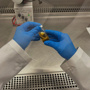 Manos con guantes revisando un vial en un laboratorio